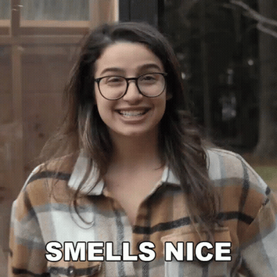 A Woman Wearing Glasses And A Plaid Shirt Smiles And Says " Smells Nice " GIF