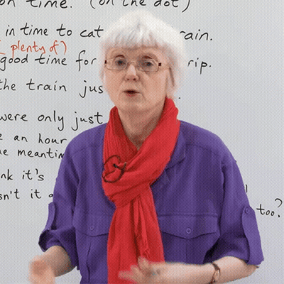 A Woman Wearing Glasses And A Red Scarf Stands In Front Of A White Board That Says " In Time To Cat " GIF