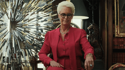 A Woman Wearing Glasses And A Red Shirt Is Sitting In Front Of A Display Of Knives GIF