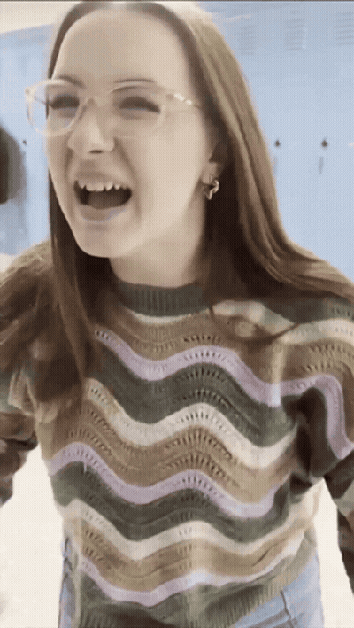 A Woman Wearing Glasses And A Striped Sweater Is Laughing With Her Mouth Open GIF