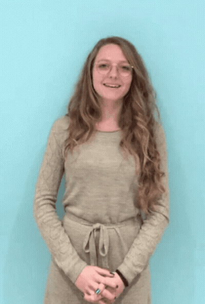 A Woman Wearing Glasses And A Tan Dress Is Smiling GIF