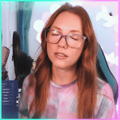 A Woman Wearing Glasses And A Tie Dye Shirt Is Sitting In Front Of A Computer Screen With The Word Tika Written On It GIF
