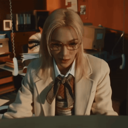 A Woman Wearing Glasses And A Tie Is Sitting In Front Of A Computer GIF