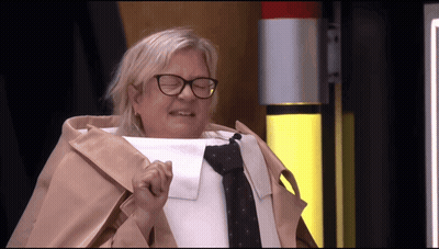 A Woman Wearing Glasses And A Trench Coat Holds Up A Piece Of Paper GIF