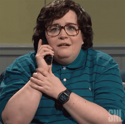 A Woman Wearing Glasses And A Watch Is Talking On A Phone With A Snl Logo In The Background GIF