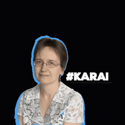 A Woman Wearing Glasses And A White Shirt Stands In Front Of A Sign That Says #Karai GIF