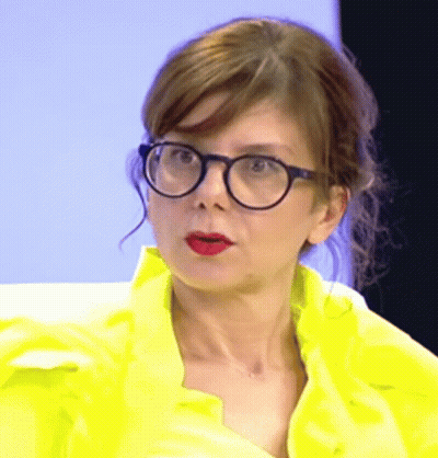 A Woman Wearing Glasses And A Yellow Jacket Is Making A Funny Face . GIF