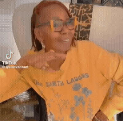A Woman Wearing Glasses And A Yellow Sweater With The Word Laughs On It . GIF