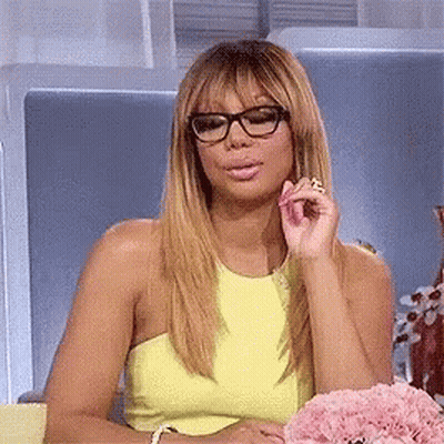 A Woman Wearing Glasses And A Yellow Top Is Sitting In A Chair . GIF