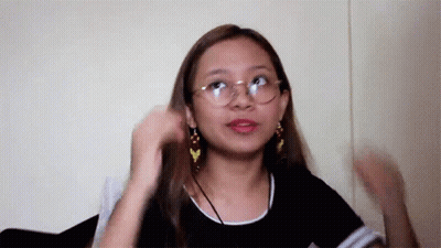 A Woman Wearing Glasses And Earrings Is Standing In Front Of A White Wall . GIF