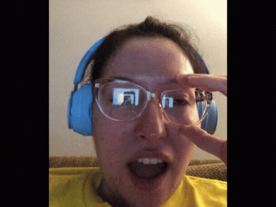 A Woman Wearing Glasses And Headphones Holds Her Hand To Her Face GIF