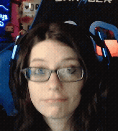 A Woman Wearing Glasses And Headphones Is Making A Face In Front Of A Sign That Says Dxracer GIF