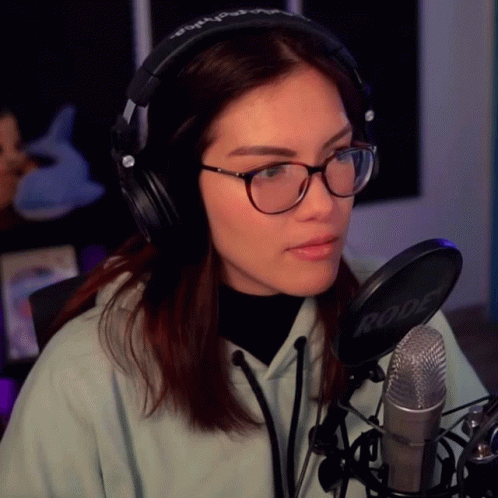 A Woman Wearing Glasses And Headphones Is Sitting In Front Of A Rode Microphone GIF