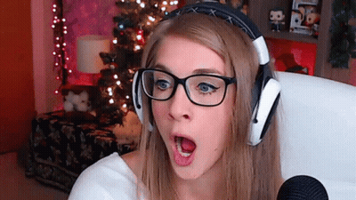 A Woman Wearing Glasses And Headphones Looks Surprised In Front Of A Christmas Tree . GIF