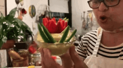 A Woman Wearing Glasses Is Holding A Glass Filled With Vegetables And Flowers . GIF