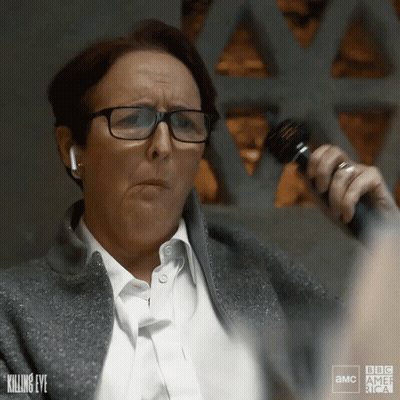 A Woman Wearing Glasses Is Holding A Microphone In Front Of A Sign That Says " Killing Eye " GIF