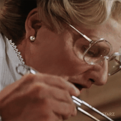 A Woman Wearing Glasses Is Holding A Pair Of Scissors In Her Mouth GIF