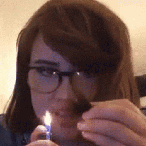 A Woman Wearing Glasses Is Lighting A Cigarette With A Blue Lighter GIF