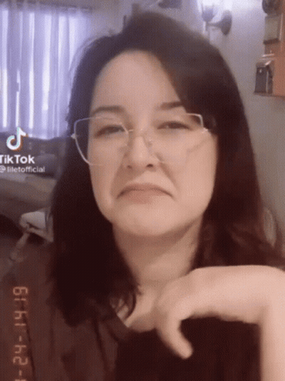 A Woman Wearing Glasses Is Making A Funny Face And Looking At The Camera . GIF