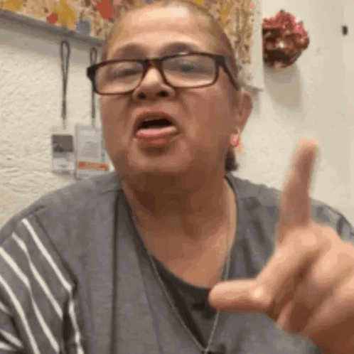 A Woman Wearing Glasses Is Making A Funny Face And Pointing Her Finger At The Camera . GIF