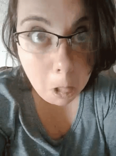A Woman Wearing Glasses Is Making A Funny Face And Sticking Her Tongue Out . GIF