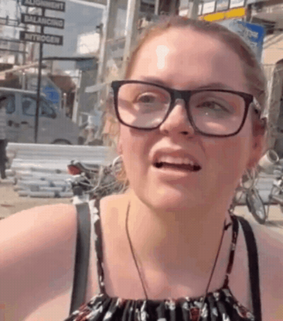 A Woman Wearing Glasses Is Making A Funny Face In Front Of A Sign That Says Balance GIF