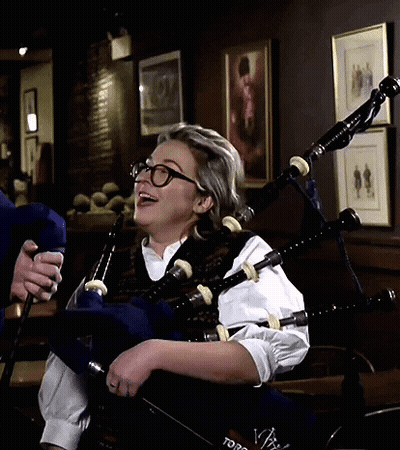 A Woman Wearing Glasses Is Playing A Bagpipe In A Room With Pictures On The Wall GIF