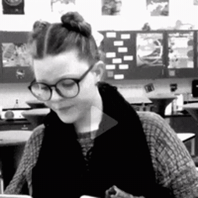 A Woman Wearing Glasses Is Sitting At A Desk In A Classroom . GIF