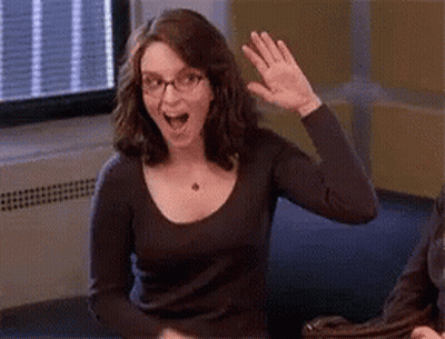 A Woman Wearing Glasses Is Sitting At A Table And Waving Her Hand . GIF