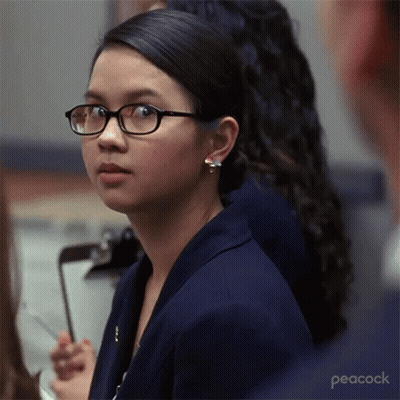 A Woman Wearing Glasses Is Sitting In Front Of A Clipboard With Peacock Written On The Bottom GIF