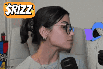 A Woman Wearing Glasses Is Sitting In Front Of A Microphone With A Sticker That Says $Rizz On It GIF