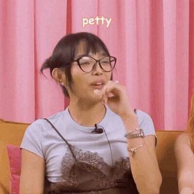 A Woman Wearing Glasses Is Sitting On A Couch And The Word Petty Is Above Her GIF