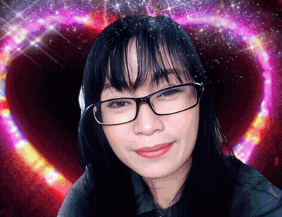 A Woman Wearing Glasses Is Smiling In Front Of A Heart GIF