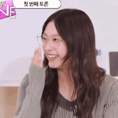 A Woman Wearing Glasses Is Smiling In Front Of A Sign That Says " Ne " GIF