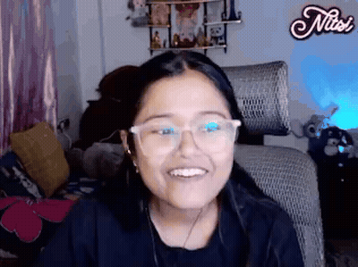A Woman Wearing Glasses Is Smiling While Sitting In A Chair In A Room . GIF