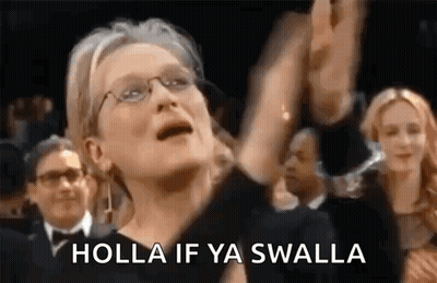 A Woman Wearing Glasses Is Standing In A Crowd With Her Arms In The Air And Says Holla If Ya Swalla . GIF