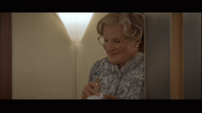 A Woman Wearing Glasses Is Standing In A Doorway GIF