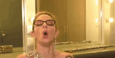 A Woman Wearing Glasses Is Taking A Selfie In Front Of A Mirror In A Room . GIF