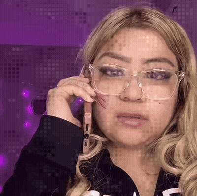 A Woman Wearing Glasses Is Talking On A Phone GIF