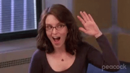A Woman Wearing Glasses Is Waving Her Hand In Front Of A Window In A Room . GIF