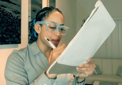 A Woman Wearing Glasses Is Writing On A Notebook GIF