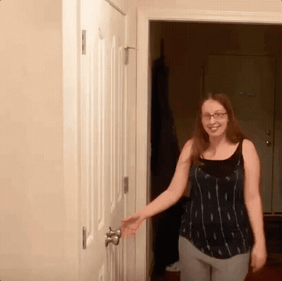 A Woman Wearing Glasses Opens A Door In A Room GIF