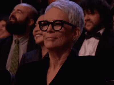 A Woman Wearing Glasses Sits In A Crowd GIF
