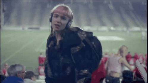 A Woman Wearing Headphones And A Backpack Is Standing On A Football Field GIF