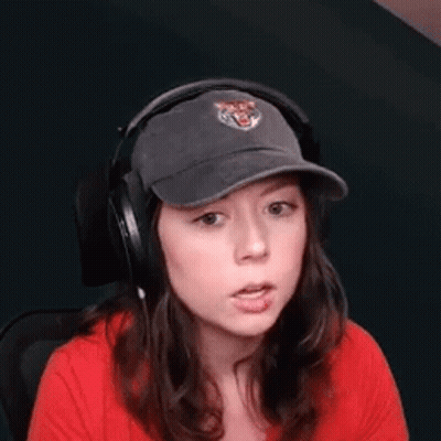 A Woman Wearing Headphones And A Baseball Cap Is Sitting In A Chair . GIF
