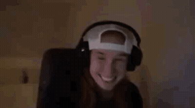 A Woman Wearing Headphones And A Baseball Cap Is Smiling And Waving . GIF