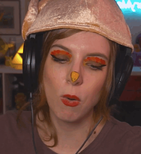 A Woman Wearing Headphones And A Chicken Hat Has A Yellow Nose GIF