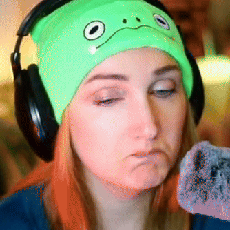 A Woman Wearing Headphones And A Green Hat With A Face On It GIF