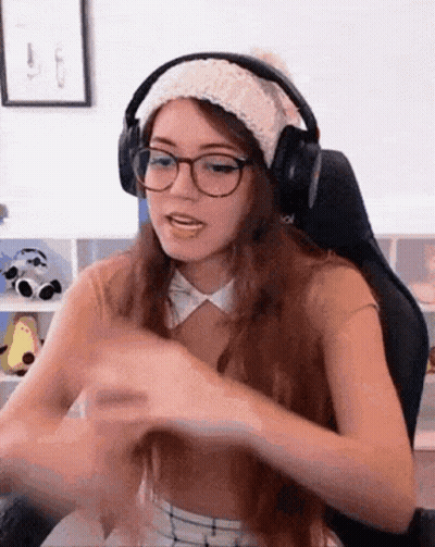 A Woman Wearing Headphones And A Hat Is Sitting In A Chair . GIF