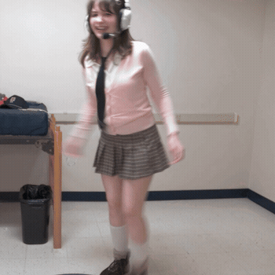 A Woman Wearing Headphones And A Pink Sweater Is Standing In A Room GIF